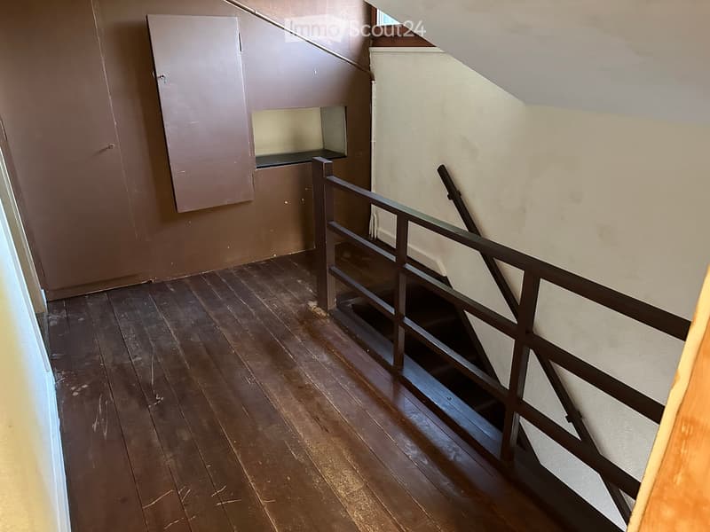 Empty hallway with wooden flooring, a metal railing leading to a staircase, and a small built-in shelf unit on the wall.