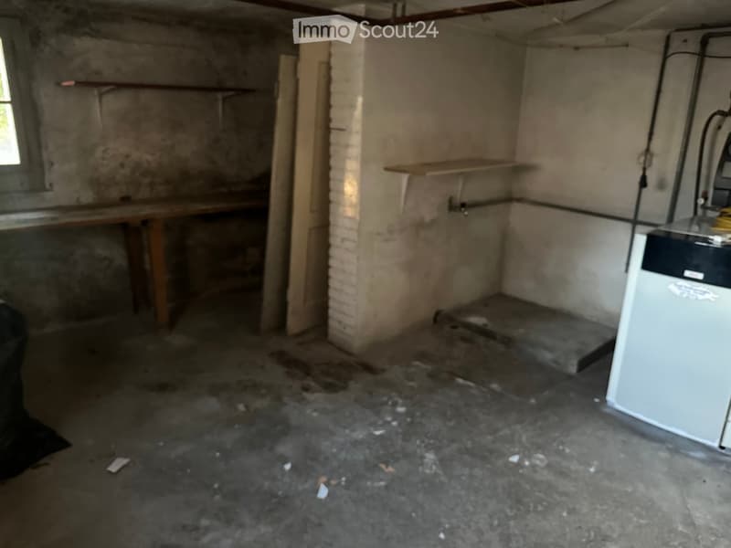 Empty basement room with concrete floor, exposed brick wall, wooden shelves, and a small window. No furniture or equipment present.