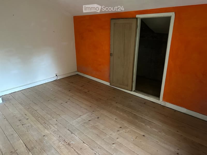 Empty room with wooden flooring, white and orange walls, and a partially open door leading to another space.
