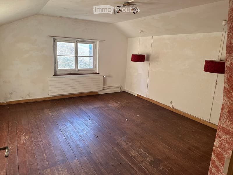 Empty room with wooden flooring, white walls, a window with a radiator below, and two hanging lamps with red shades.