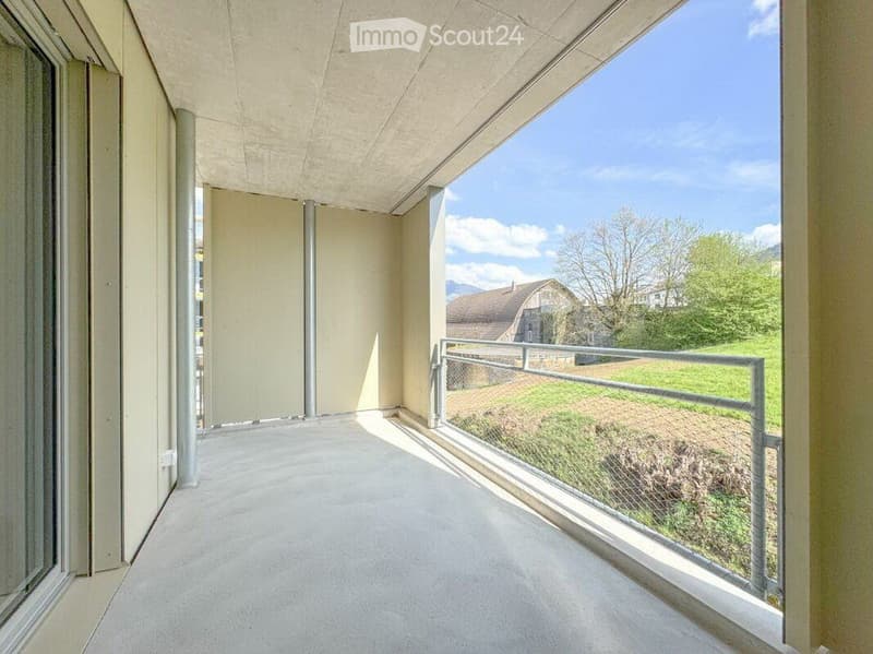 Modern balcony with concrete floor, glass sliding doors, metal railing, and scenic mountain view.