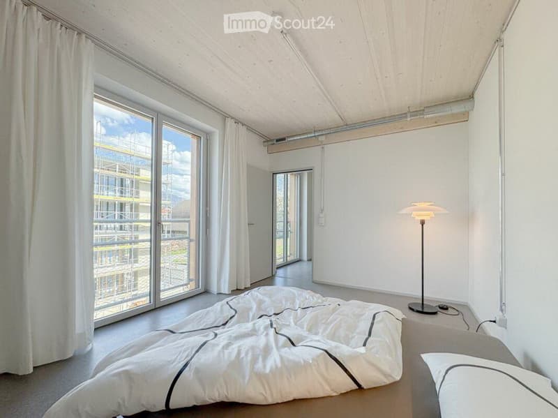 Modern, minimalist bedroom with large windows, white bedding, and a floor lamp.