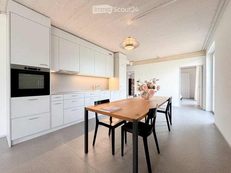 Modern kitchen with white cabinets, a wooden dining table, black chairs, and a vase with flowers on the table.