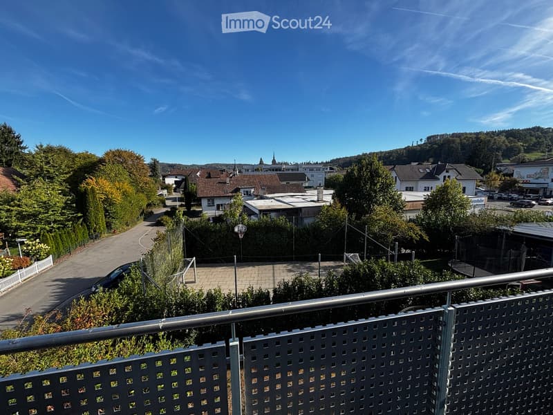 Balcony overlooking a residential area with houses, trees, and a clear blue sky.