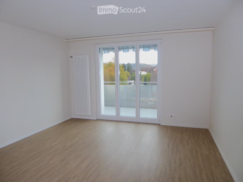 Empty room with wooden flooring, white walls, and large sliding glass doors leading to a balcony.