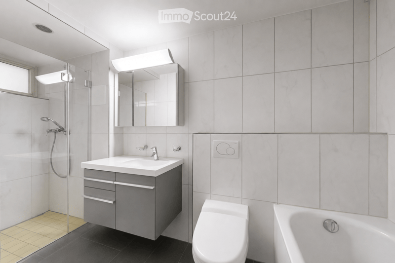 Modern bathroom with white tiles, a sink with a mirror, a toilet, a bathtub, and a glass-enclosed shower area.