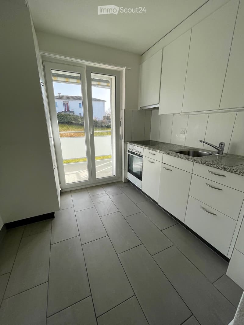 Modern kitchen with white cabinets, granite countertop, built-in oven, and a large sliding glass door leading to the outdoor area.