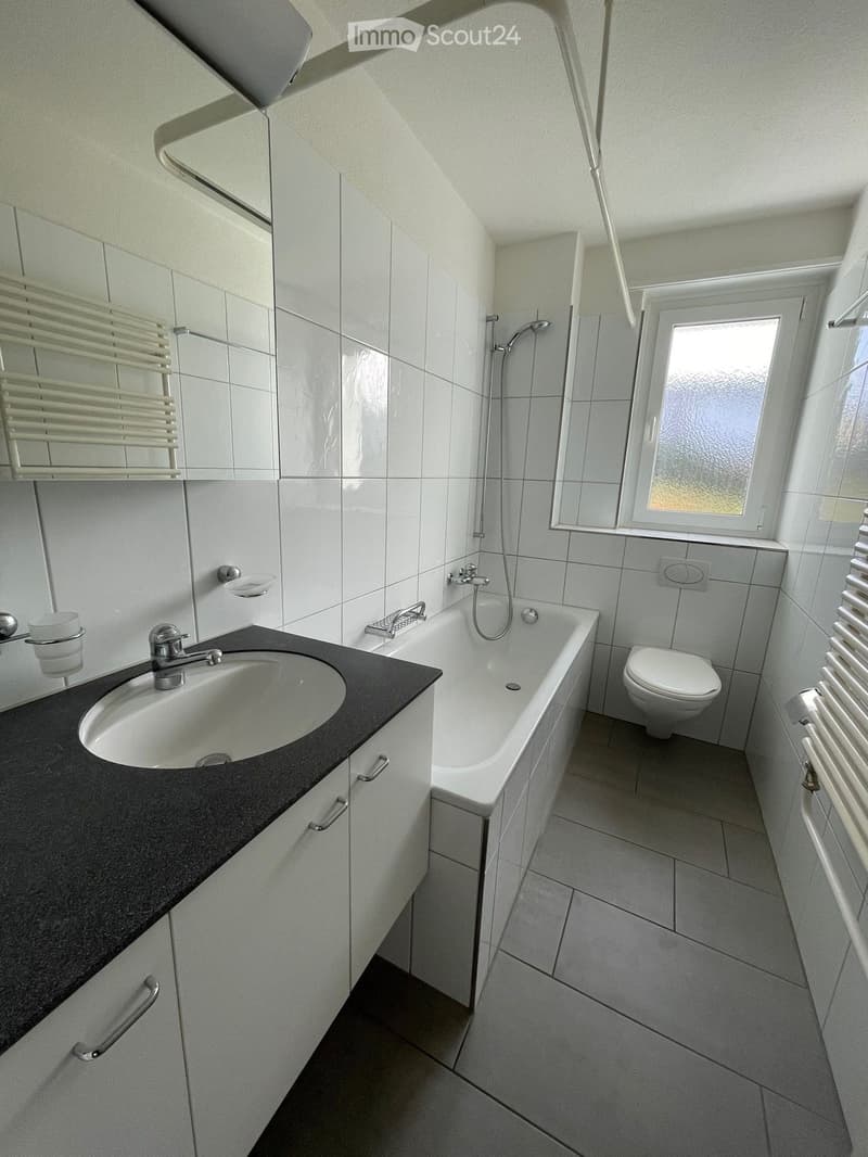 Modern bathroom with white tiles, a black countertop sink, a bathtub, a toilet, and a radiator.