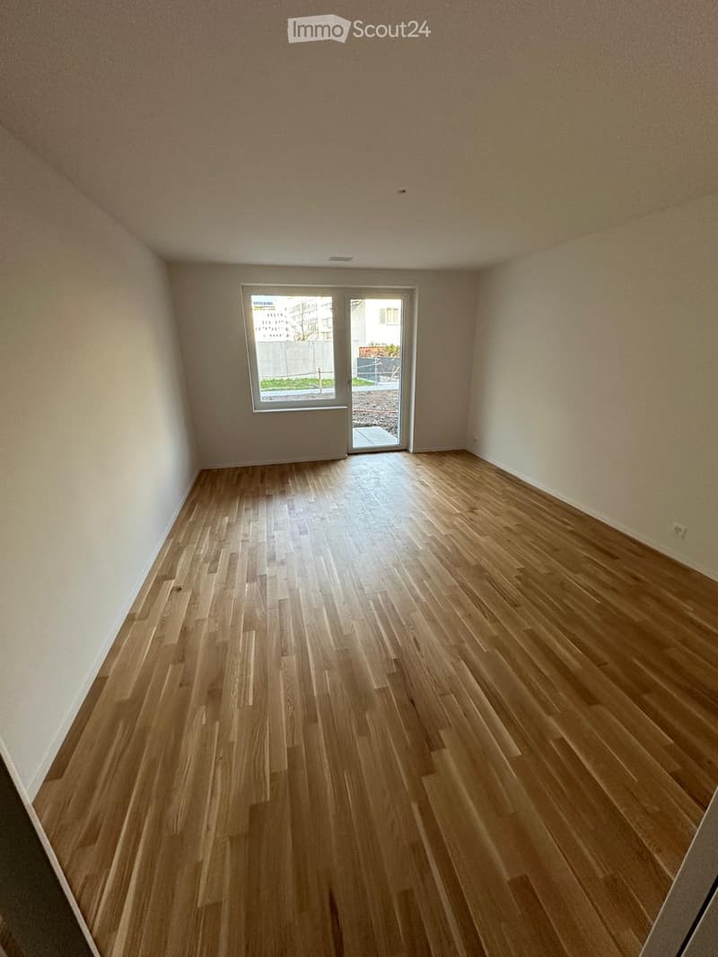 Empty room with wooden flooring and white walls, featuring a large window and a sliding glass door leading to an outdoor area.