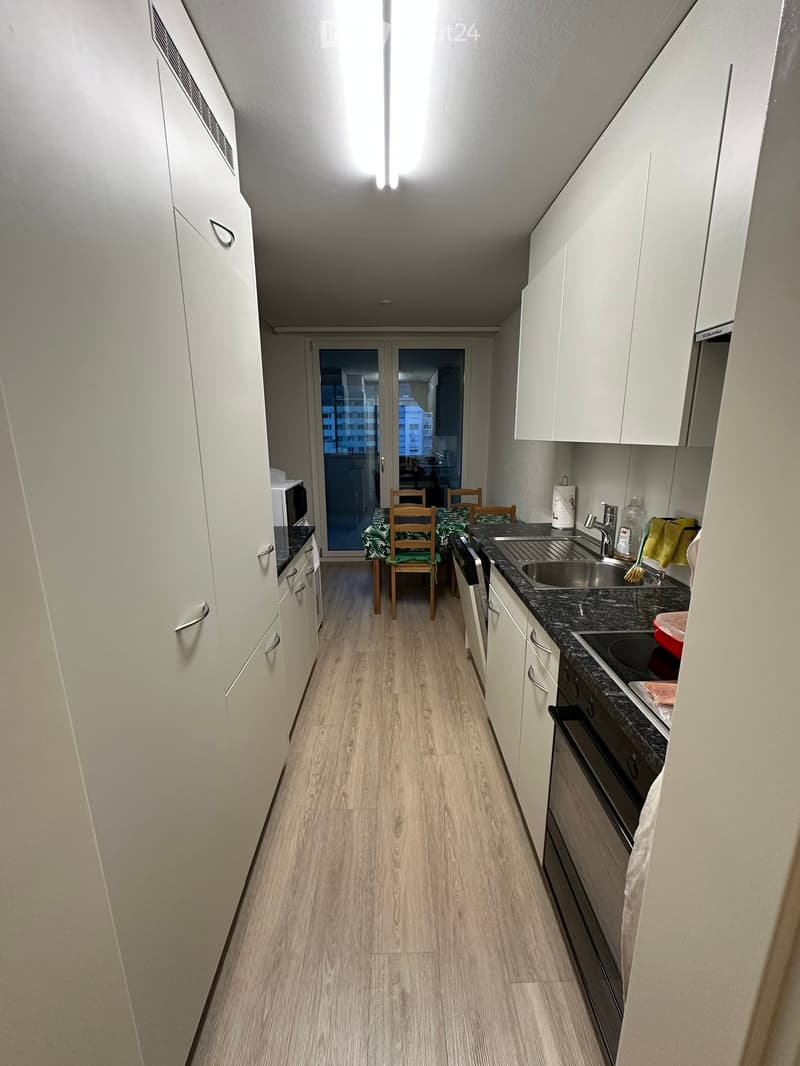 Modern kitchen with white cabinets, granite countertops, and a small dining area with a table and chairs. The space features a microwave, sink, and oven.
