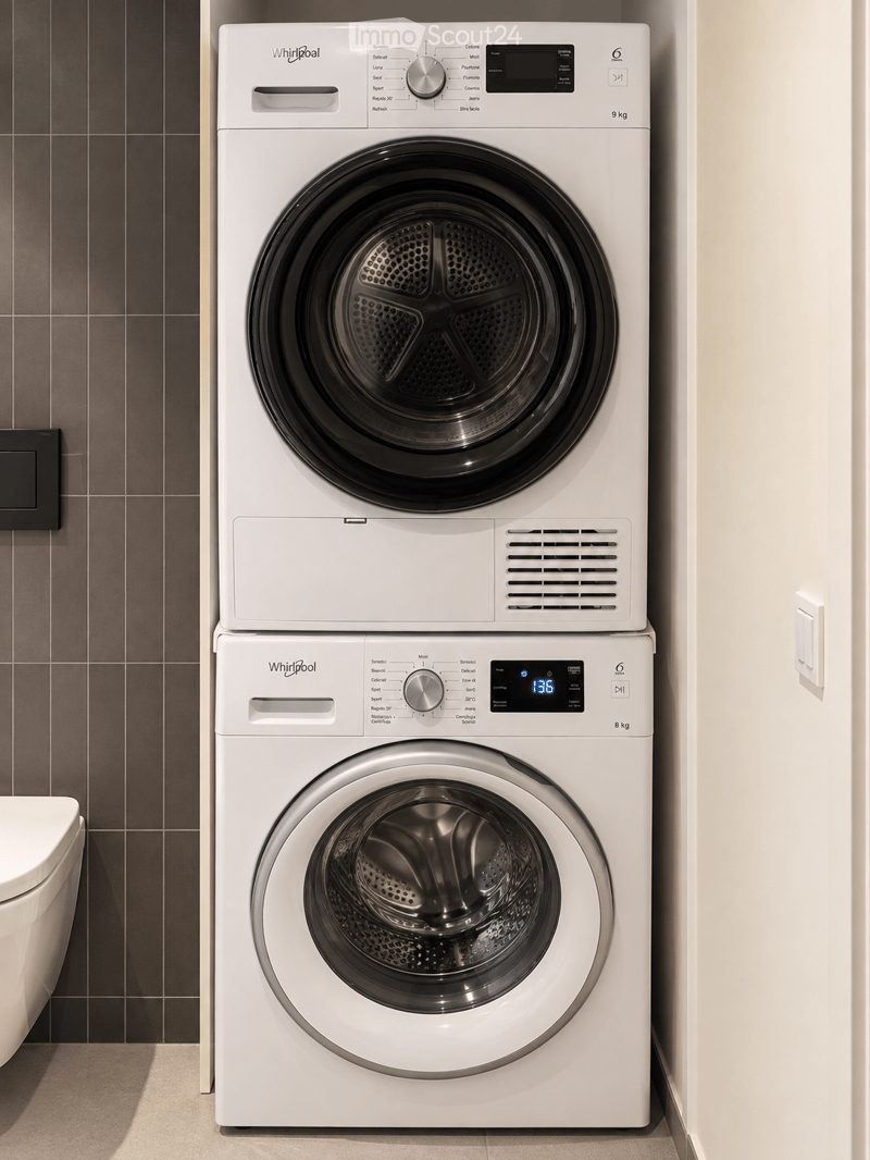 Modern bathroom with a white Whirlpool washing machine and dryer stacked vertically, a toilet, and dark tiled walls.