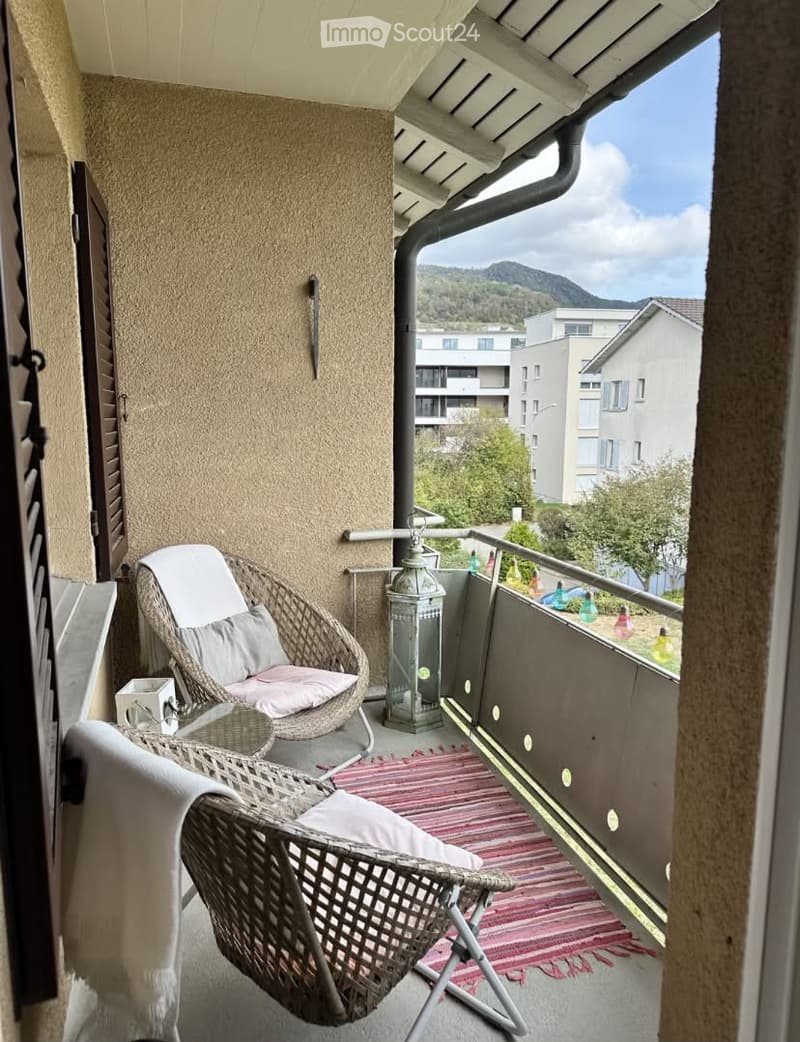 Balcony with a view of mountains, featuring two wicker chairs, a small table, and a lantern.