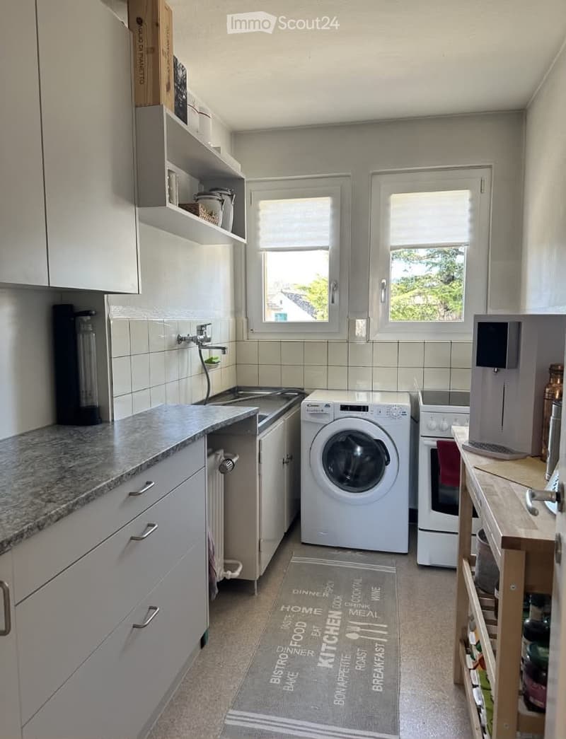 Modern kitchen with white cabinets, granite countertop, sink, washing machine, oven, coffee maker, and shelves.