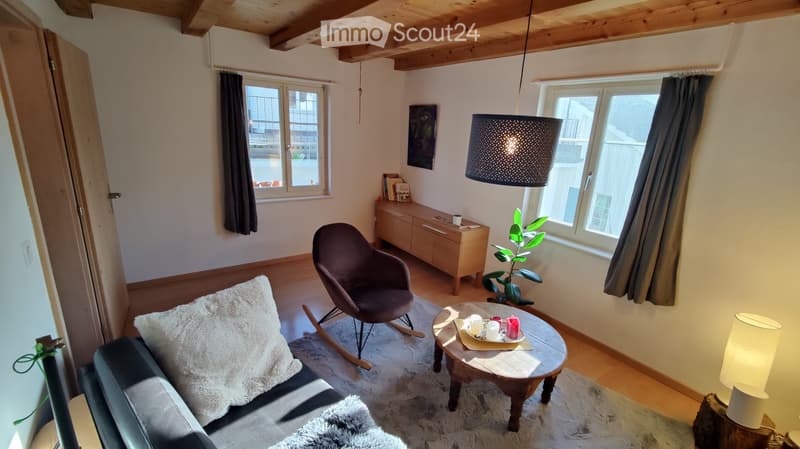 Cozy living room with a dark leather sofa, a rocking chair, a wooden coffee table, a sideboard, and a hanging lamp.