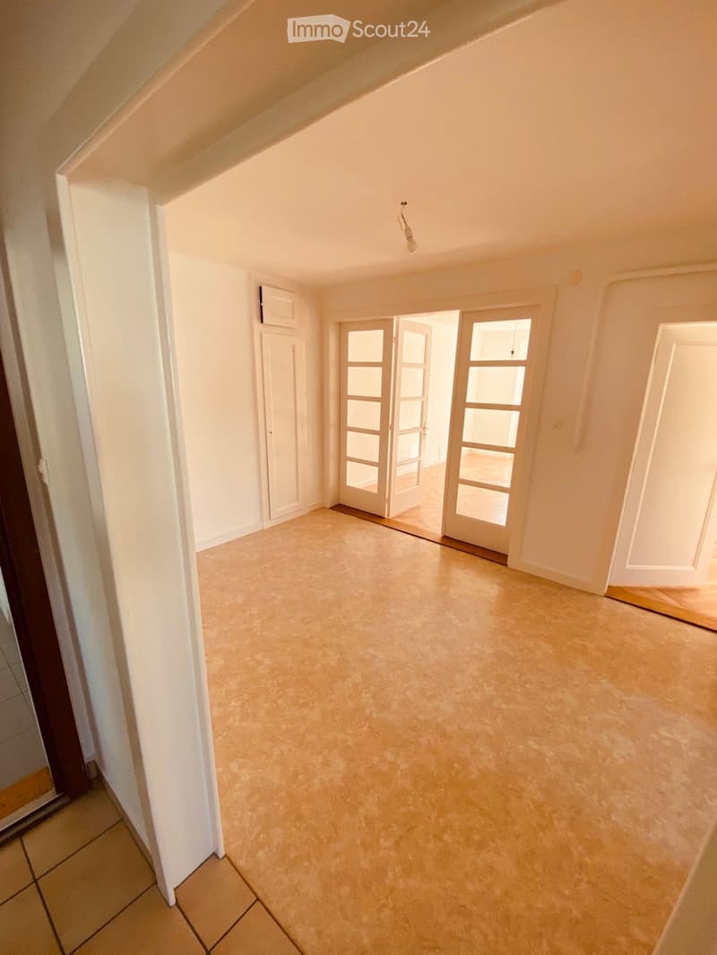 Empty hallway with beige tiled floor, white walls, and multiple doors including a sliding glass door leading to another room.