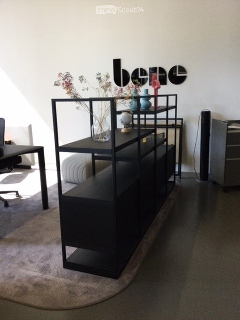 A modern, minimalist living room with a black shelving unit, a round chair, a small table, and decorative vases.