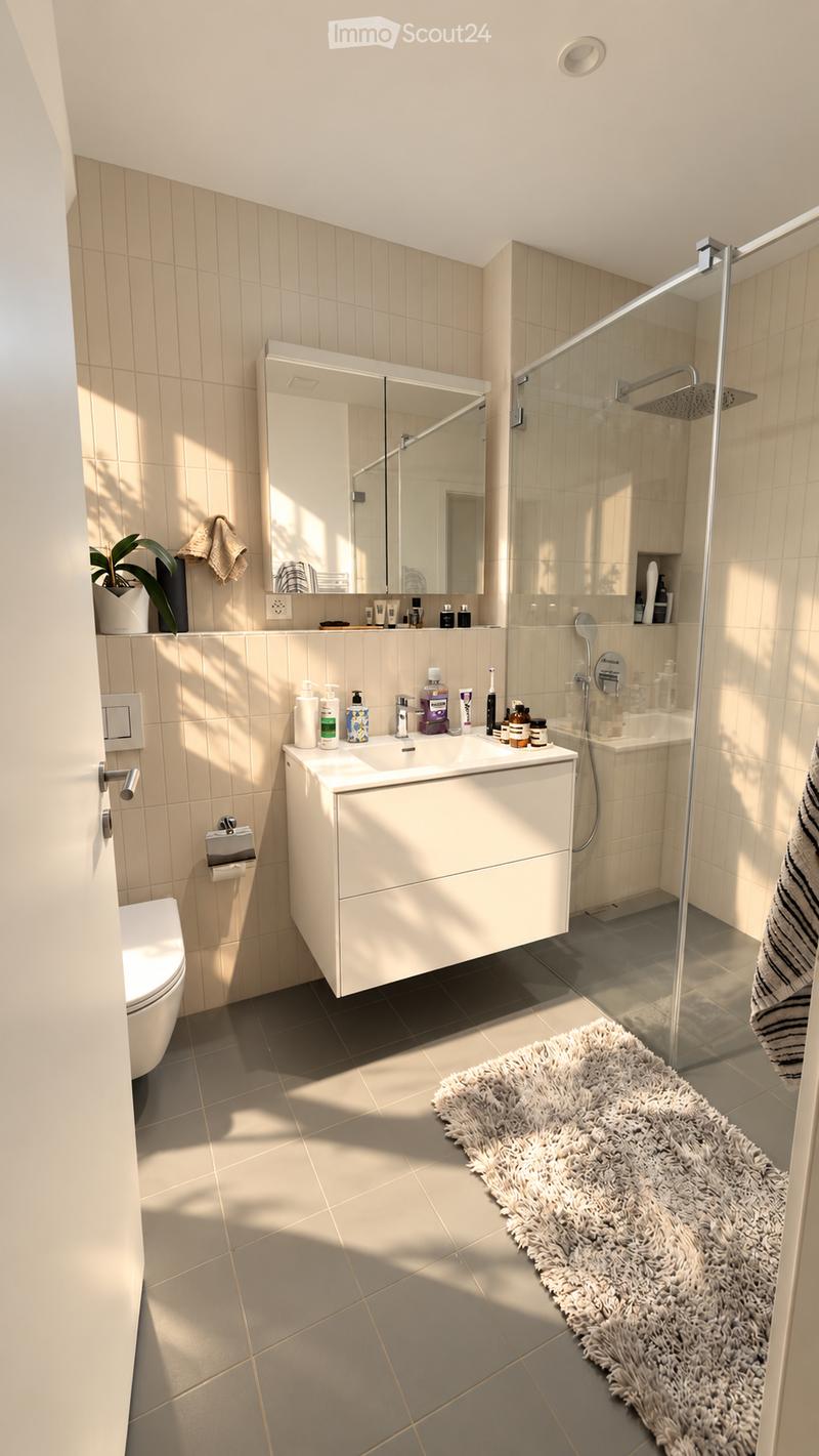 Modern bathroom with a white sink, mirror, toilet, and glass-enclosed shower. Features a fluffy white rug, a potted plant, and various toiletries on the sink counter.