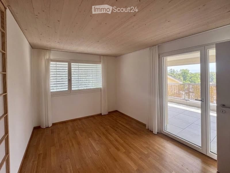 Empty room with wooden flooring, white walls, large window with blinds, and sliding glass door leading to a balcony.