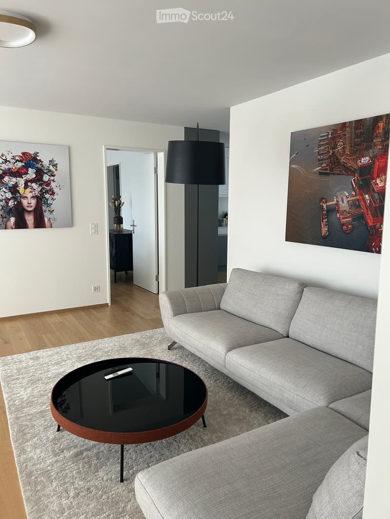 Modern living room with a grey sectional sofa, round coffee table, floor lamp, and artwork on the walls.