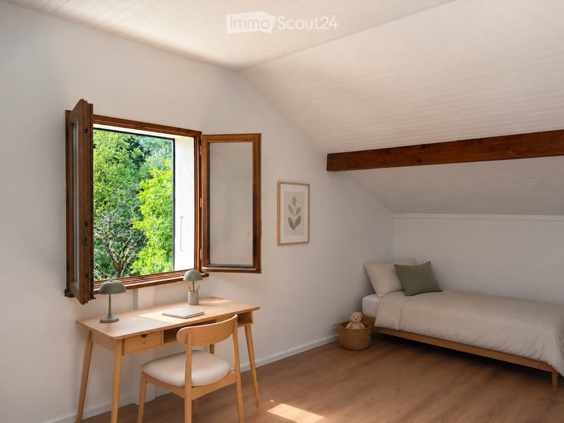 Cozy bedroom with a slanted ceiling, wooden bed, desk, chair, and a large window offering a view of greenery.