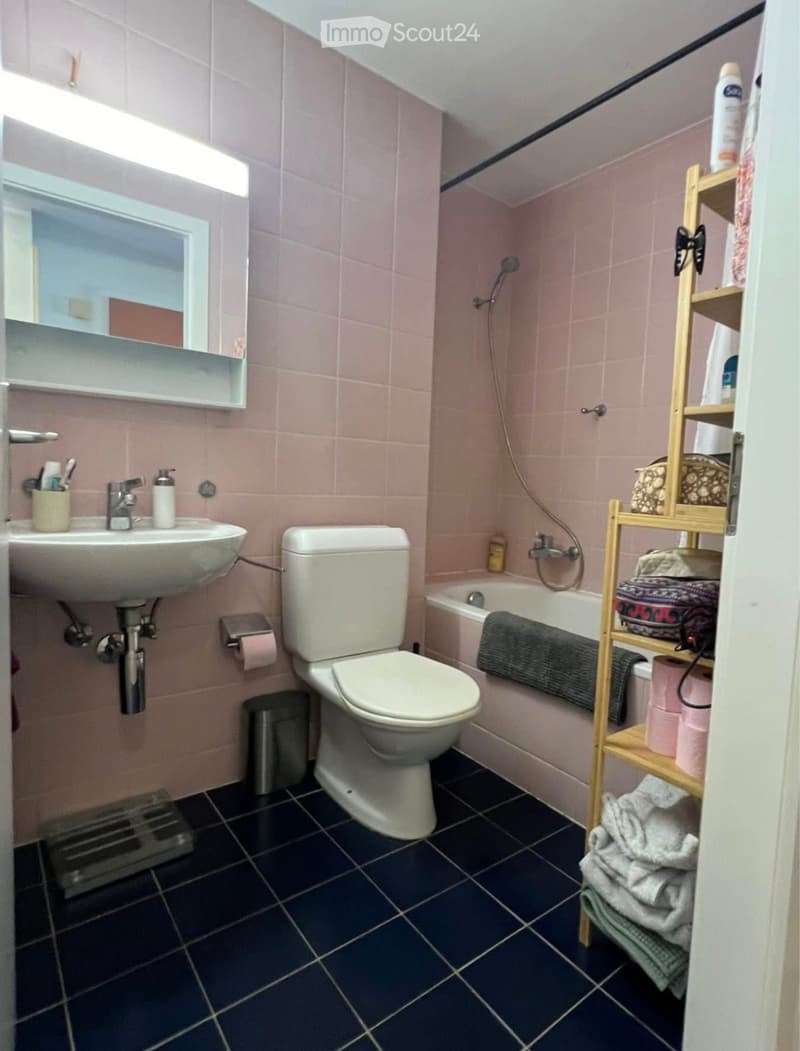 Bathroom with pink tiles, a white sink, toilet, bathtub, and a wooden towel rack holding towels and toiletries.