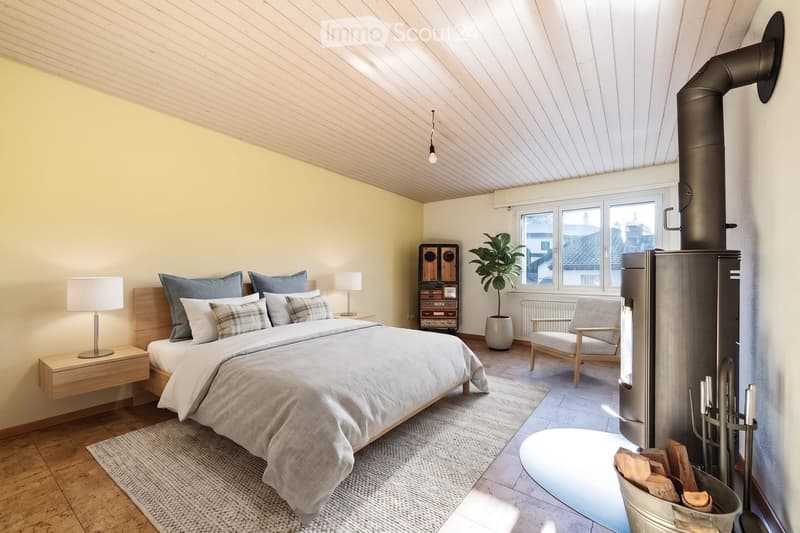 Modern bedroom with a large bed, nightstands, lamps, a cozy chair, a potted plant, and a fireplace with wood storage.