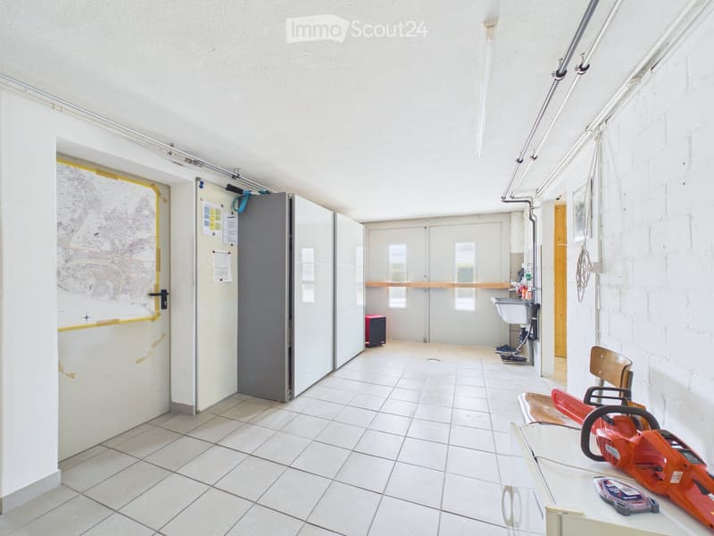 A clean, tiled room with a sink, a chair, a table holding a chainsaw, and a cabinet. The room has white walls and a door with a map on it.