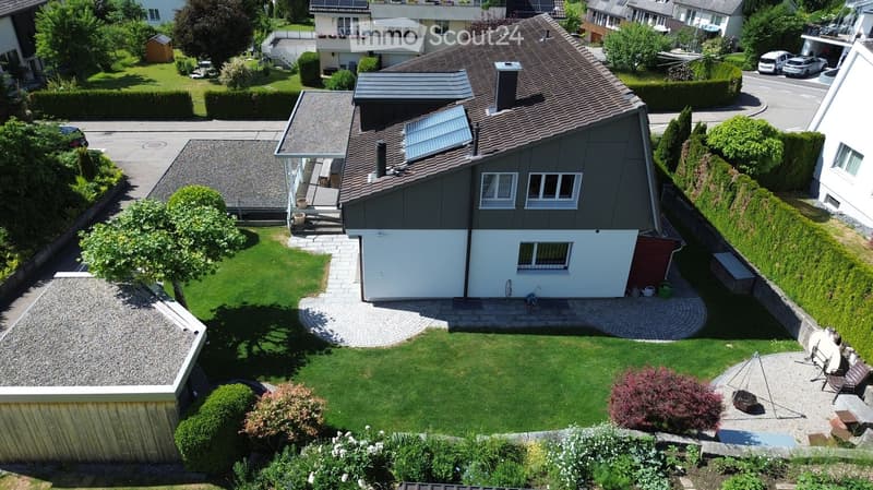 Aerial view of a residential house with a well-maintained garden, patio, and surrounding neighborhood.