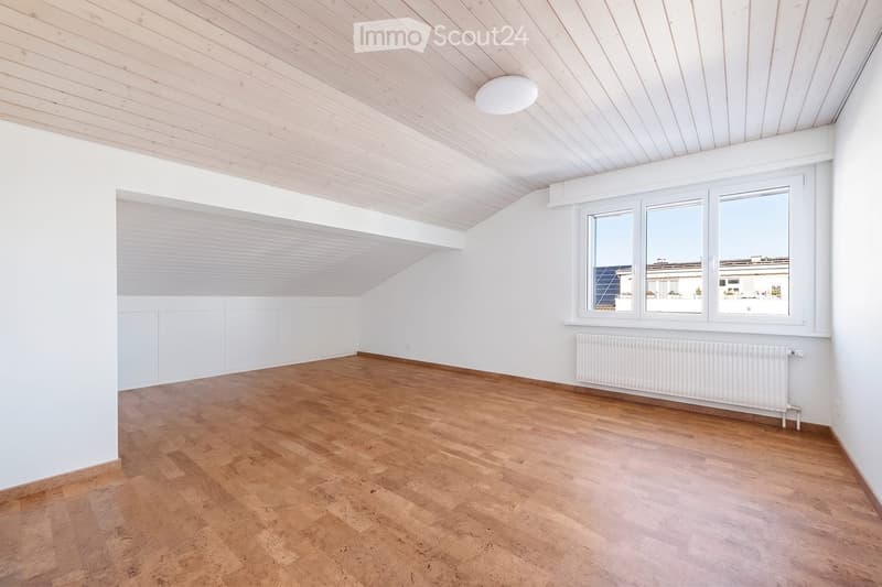 Empty room with wooden flooring, white walls, and a slanted wooden ceiling. Features large windows and a radiator.
