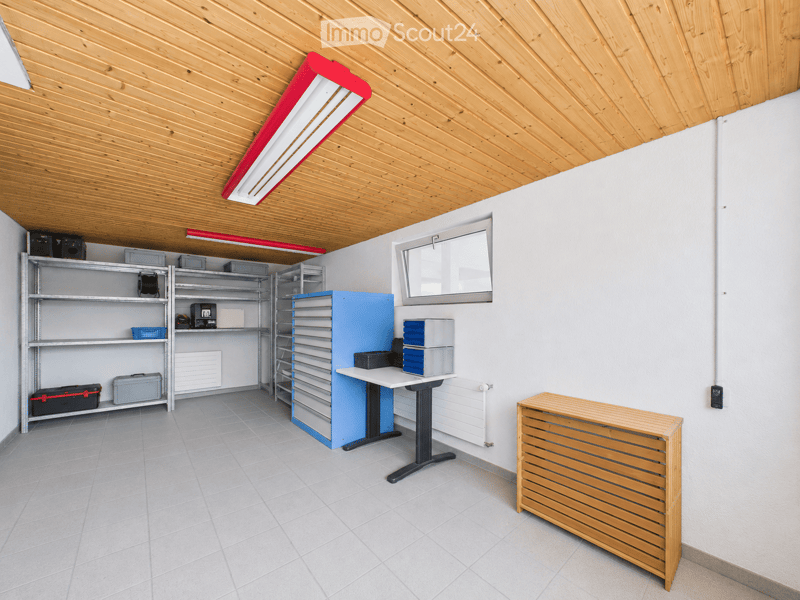 A well-lit, organized room with wooden slatted ceiling, tiled floor, metal shelving units, a standing desk, and a wooden radiator.