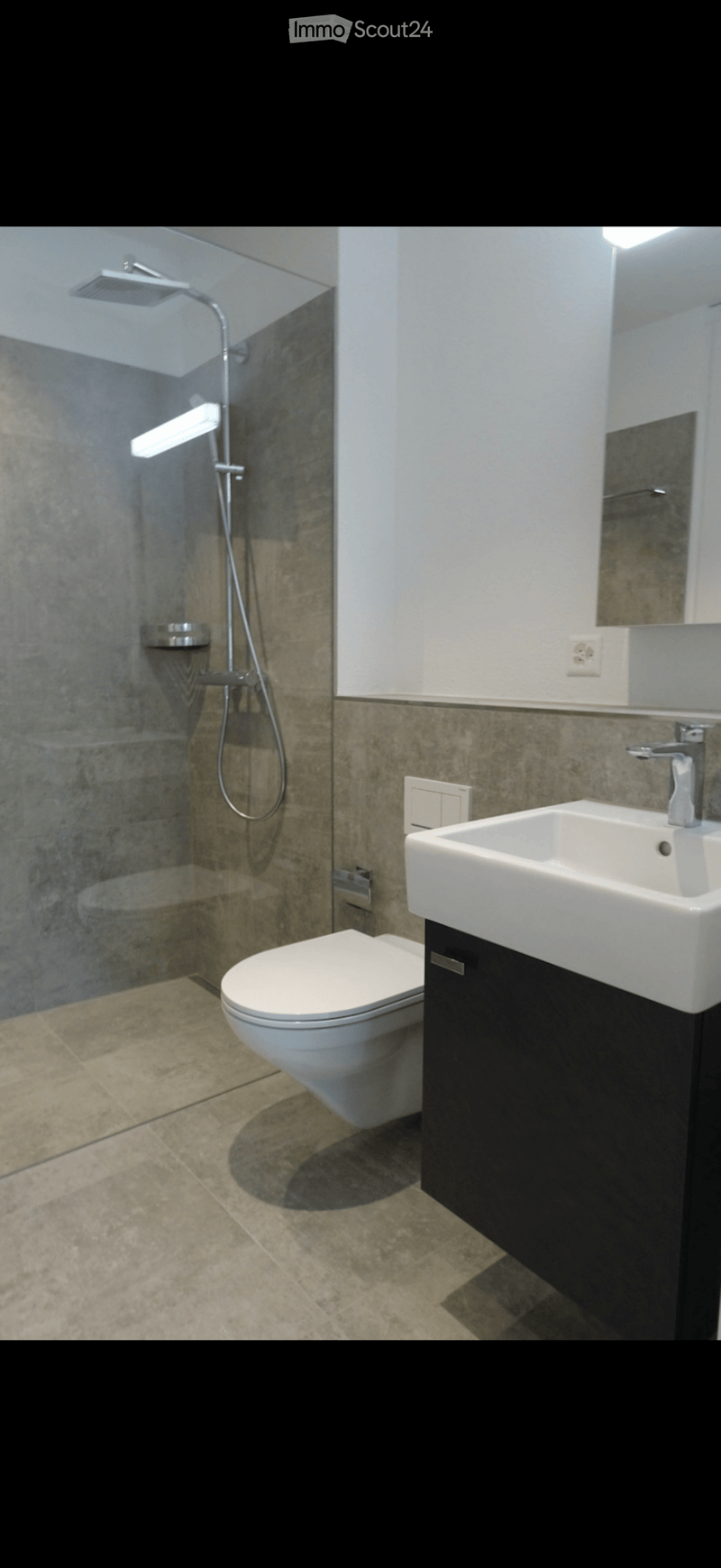 Modern bathroom with a toilet, sink, and glass-enclosed shower. Features a sleek design with dark tiles and a white sink.
