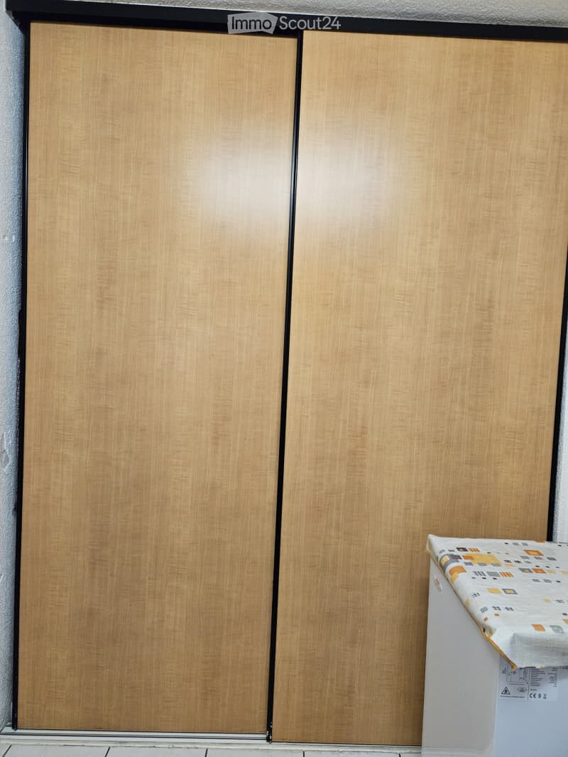 A small room with a wooden cabinet and a refrigerator covered with a colorful cloth.
