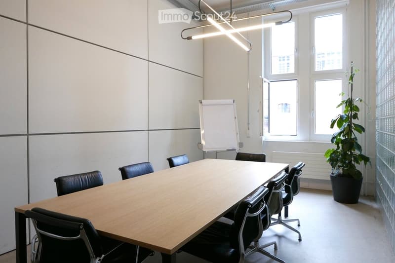 Modern conference room with a large wooden table, black chairs, a whiteboard, and a potted plant near the window.