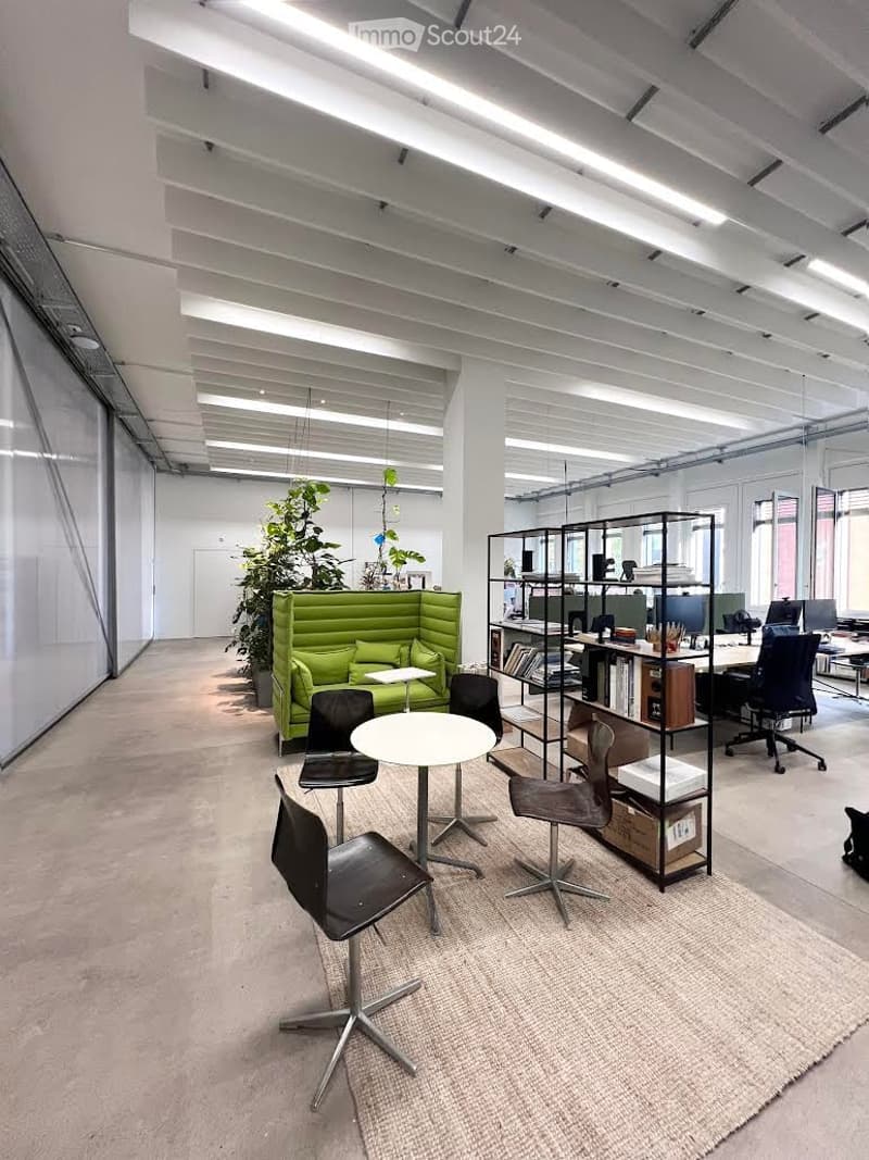 Modern office space with a green sofa, white round table, black chairs, shelving units, and multiple computer screens.