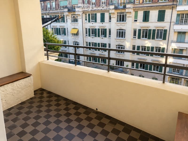 Balcony with checkered tile flooring, metal railing, and a view of surrounding buildings with green shutters.