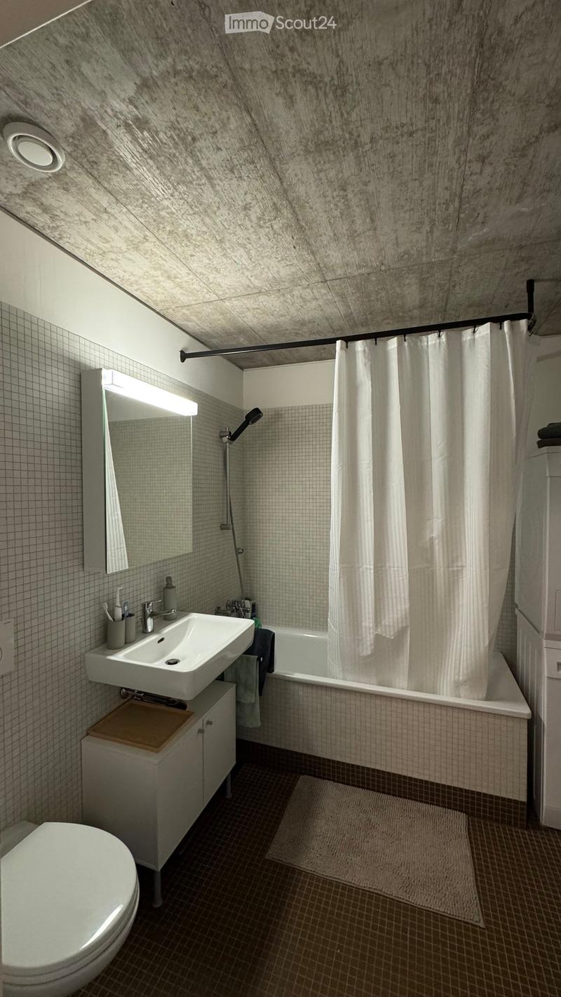 Modern bathroom with a white sink, toilet, bathtub, and mirror. Features a shower curtain, tiled walls, and a small cabinet under the sink.