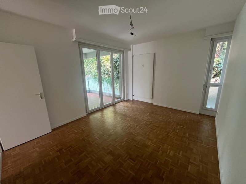 Empty room with wooden flooring, large sliding glass doors, and white walls.