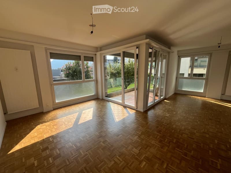 Empty room with wooden parquet flooring, large windows, and sliding glass doors leading to a balcony or terrace area.