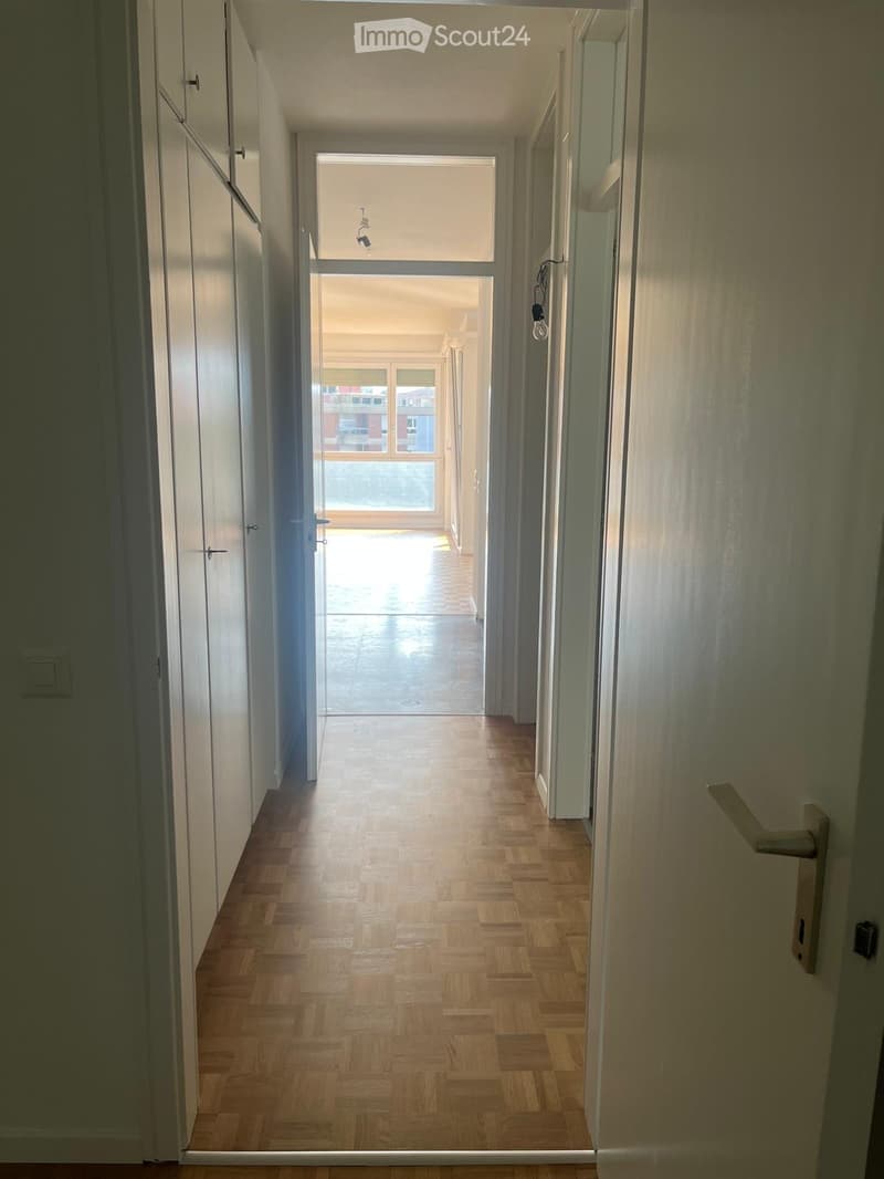 Empty hallway with wooden flooring, white walls, and multiple doors leading to other rooms.
