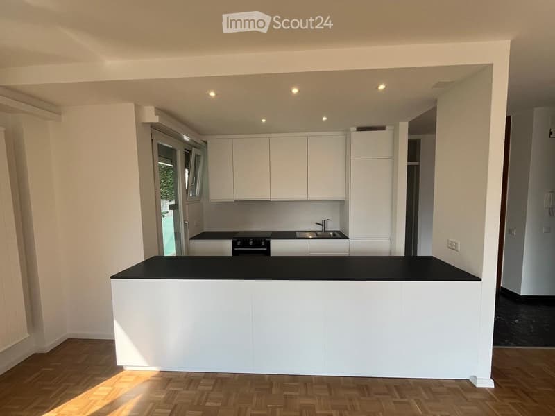 Modern kitchen with white cabinets, a black countertop island, and built-in appliances including a stove and sink.