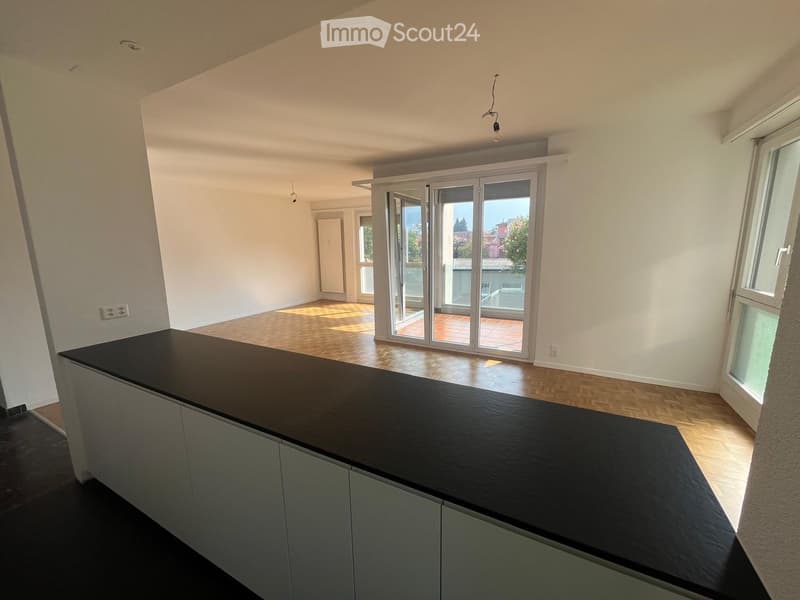 Modern kitchen with a black countertop, grey cabinets, and wooden flooring. Large sliding glass doors lead to a balcony.