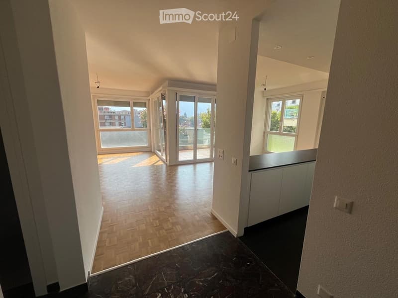 Empty hallway with wooden flooring and large windows leading to a balcony area.