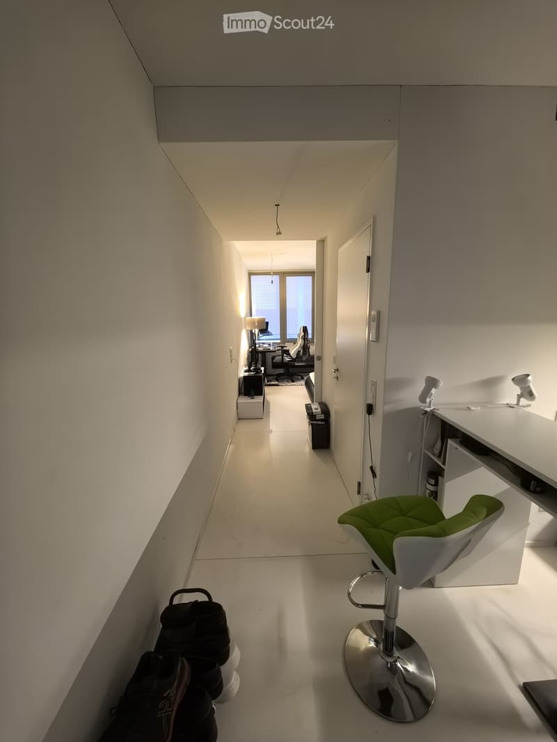 Modern hallway with white walls, polished floor, and built-in storage. A green stool and a backpack are visible.