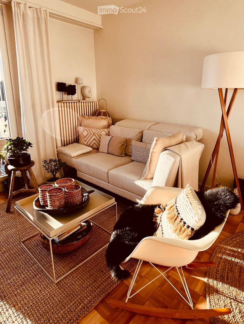 A modern living room with a light-colored sofa, coffee table, white armchair, floor lamp, and decorative items including a plant and a sculpture on the mantel.