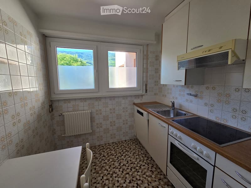 The kitchen features a tiled backsplash, wooden countertops, a sink, stove, oven, and cabinets. There is a window with a view of greenery outside.