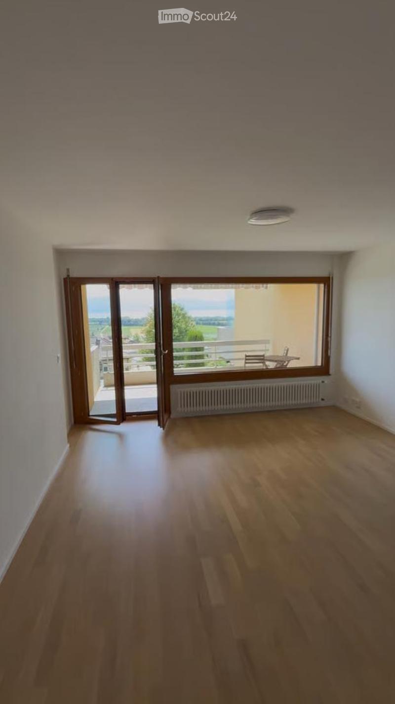 Empty room with wooden flooring, large windows, and a sliding door leading to a balcony.