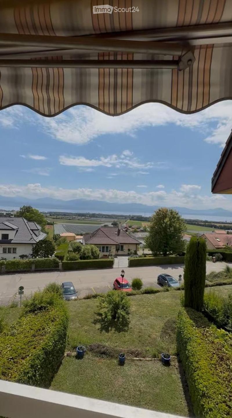 Balcony with striped awning, overlooking a landscaped garden, parking area, and distant mountains.