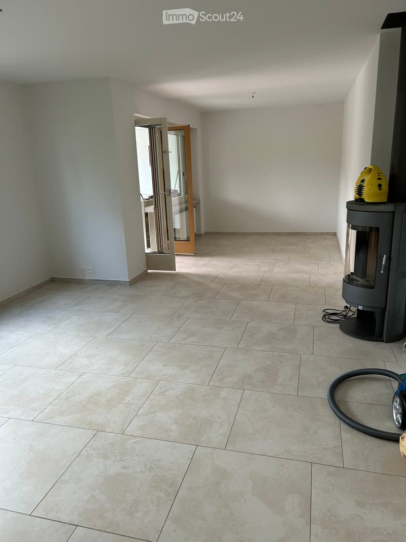 Empty room with tiled floor and white walls, featuring a fireplace and a vacuum cleaner in the corner.