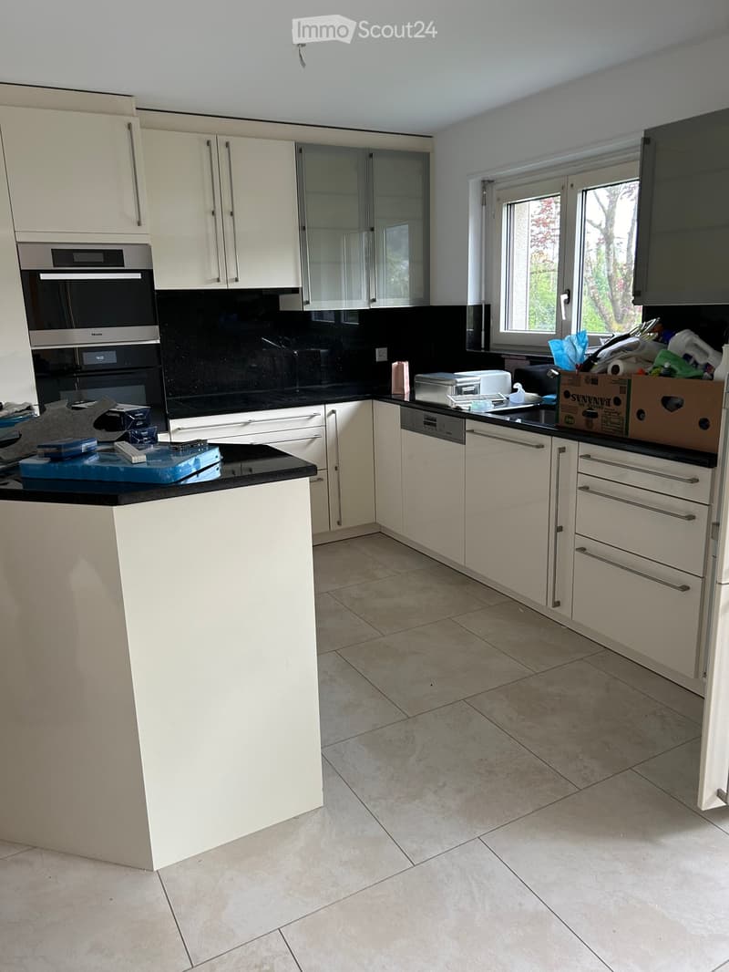 Modern kitchen with white cabinets, black countertops, and stainless steel appliances including an oven and dishwasher. The space features a large window and a central island.