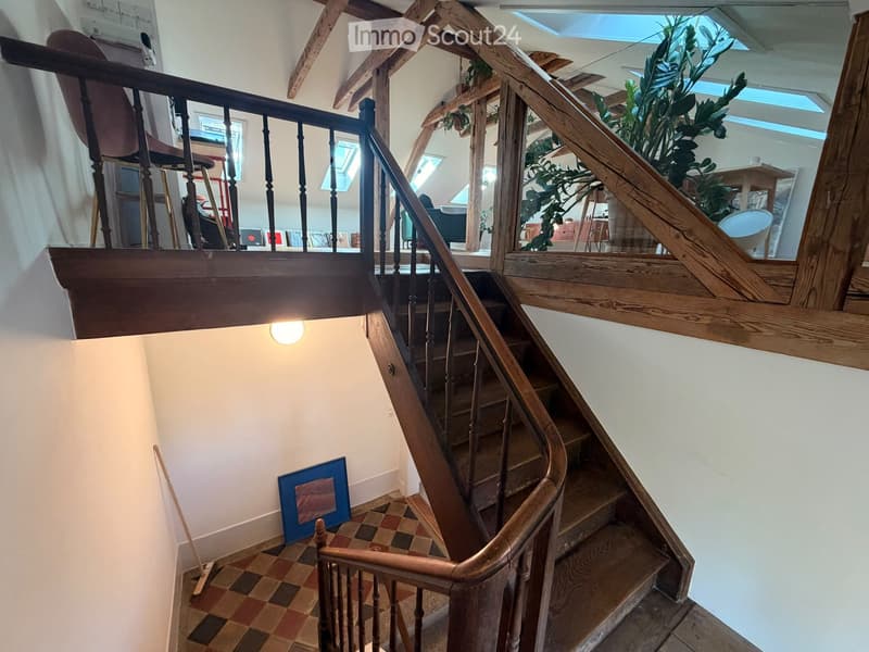 Spiral staircase with wooden railings and steps, leading to an upper level with visible rooms and plants.
